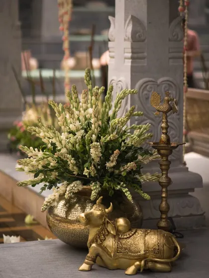 Traditional elements bring a sense of sanctity and grace. A brass Nandi statue and a traditional lamp sit beside a floral arrangement, adding a touch of royal, cultural elegance to the wedding decor.