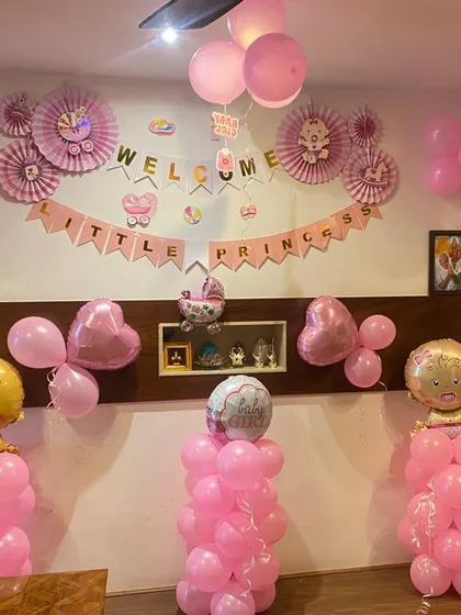 A 'Welcome Little Princess' home decoration. The room is filled with pink balloons, paper fans, and balloon columns topped with baby girl foil balloons.