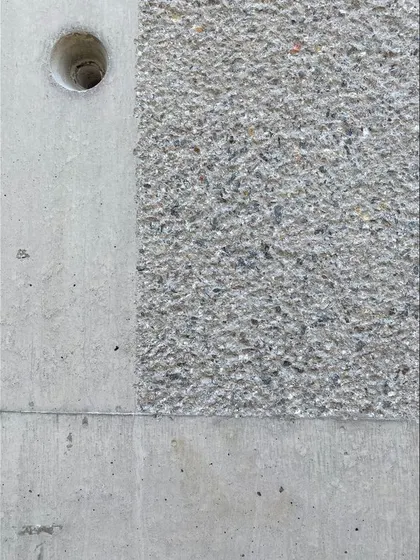 A close-up detail showing the contrast between a smooth, off-form concrete finish and the rough texture of a bush-hammered section.