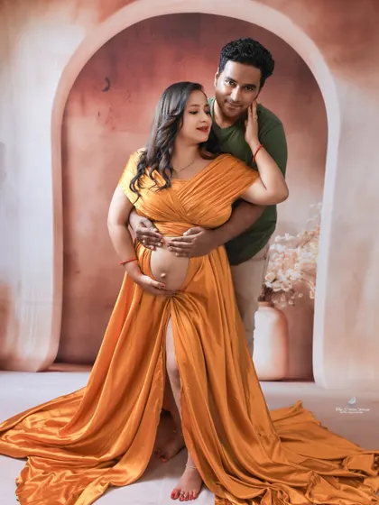 An intimate pose showing the couple's connection. The father-to-be's hands gently rest on his partner's, who is glowing in a beautiful yellow satin gown.