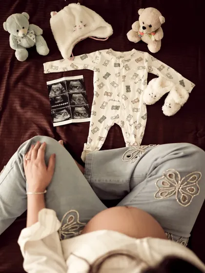 An overhead shot of the mom-to-be with a beautiful arrangement of baby clothes, sonogram pictures, and teddy bears, creating a lovely flat lay effect.