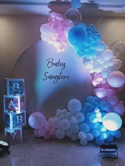 A creative gender reveal decoration using pink and blue lighting on a white balloon arch. This setup, with 'BABY' blocks and a simple backdrop, keeps the surprise until the final color is revealed.