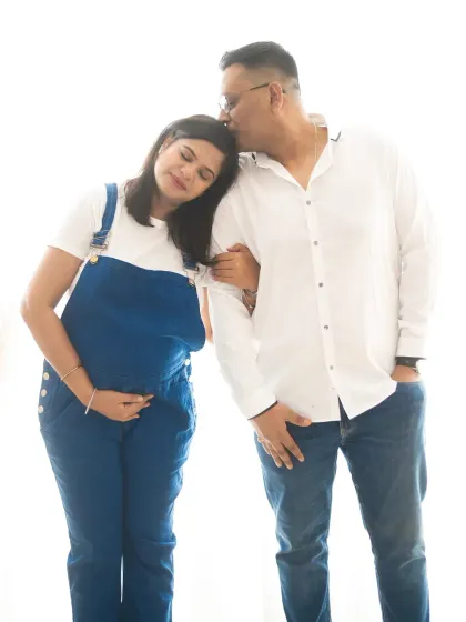A tender moment between an expecting couple in a casual, relaxed style. The denim overalls and white shirt create a fresh and modern look.