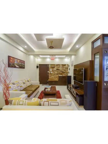 This living room features a more traditional Indian design aesthetic, with a wooden media unit and a textured stone accent wall. The space feels warm, familiar, and rooted in culture.