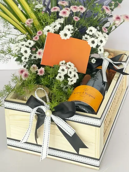 A detailed shot of the alcohol hamper, showing the bottle of champagne and a blank card for your personal message, surrounded by fresh flowers and greenery.