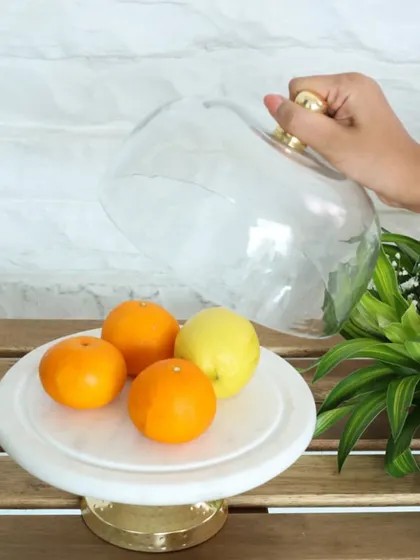 Lifting the glass cloche to reveal fresh citrus on our white marble and gold cake stand. This piece is as functional as it is beautiful, perfect for any modern kitchen.