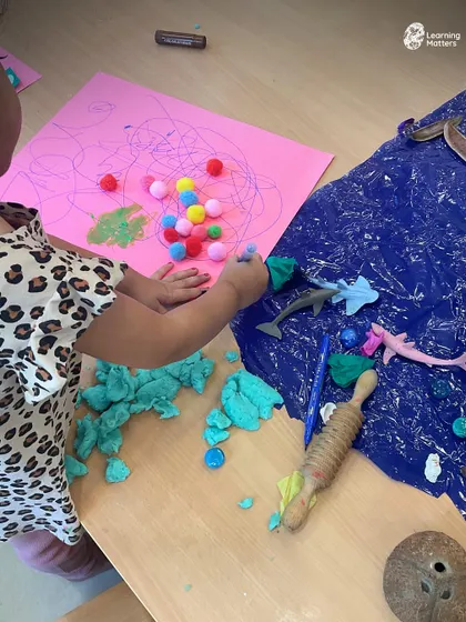 This invitation to play combines multiple textures: soft pom-poms, squishy playdough, and smooth plastic animals. Offering a variety of materials allows children to make choices and lead their own sensory exploration.