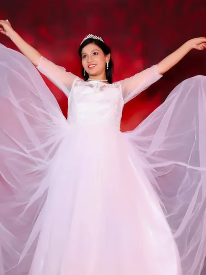 A joyful maternity portrait of a woman in a white gown with flowing fabric wings, celebrating her pregnancy.