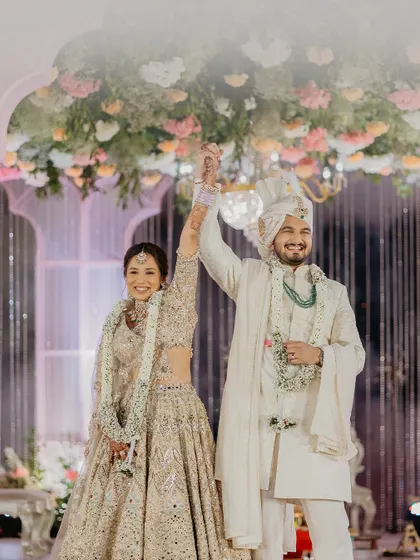 A triumphant and happy moment after the wedding ceremony, with the couple raising their hands in celebration under a canopy of flowers.