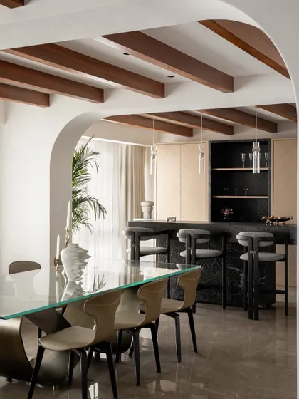 A well-designed dining and bar area becomes the heart of the home. Here, I combined a sleek glass dining table with a dark marble bar and exposed wooden ceiling beams to balance modern elegance with a warm, earthy feel, perfect for entertaining.