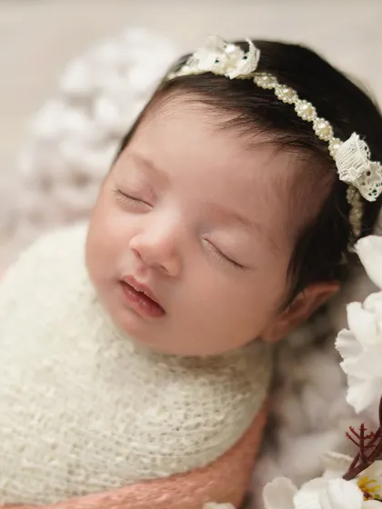 A sweet close-up of a newborn's face, framed by white flowers. The focus on her delicate features and lace headband makes for a truly precious memory.