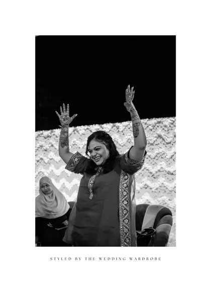 A black and white portrait of the bride, her hands raised in celebration during her Mehendi.