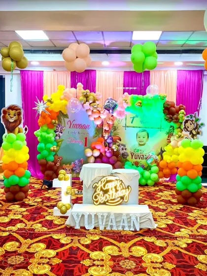 The main stage of a jungle-themed first birthday party. The setup is rich with details, including animal cutouts, a custom backdrop, and a "Happy Birthday" marquee sign.