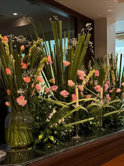 A close-up of a bar arrangement for an 80th birthday party. The mix of tall green leaves and soft pink carnations, interspersed with candles, adds elegance to every corner of the event.