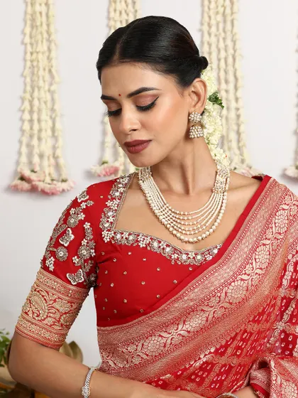 A close-up of a beautiful red Banarasi Bandhani saree, paired with a heavily embroidered blouse.
