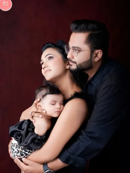 A classic family portrait with a newborn, showcasing the love and protection of new parents. The dark background makes the moment feel intimate and focused.