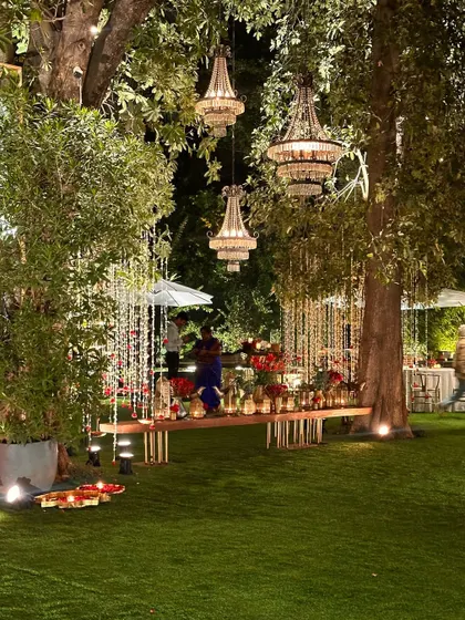 A long table setup on the lawn, with chandeliers hanging from the trees above.