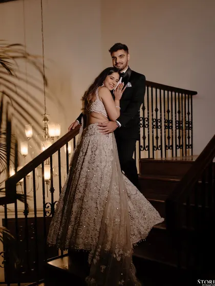 An elegant portrait on a grand staircase. The classic tuxedo and shimmering lehenga create a look of timeless Hollywood glamour for this engagement shoot.