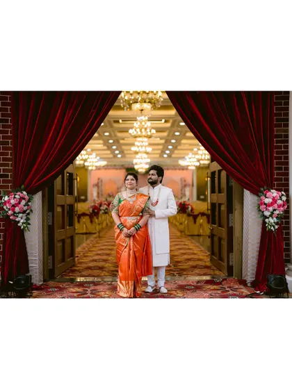A grand, wide shot of the couple framed by dramatic red curtains at their wedding venue.