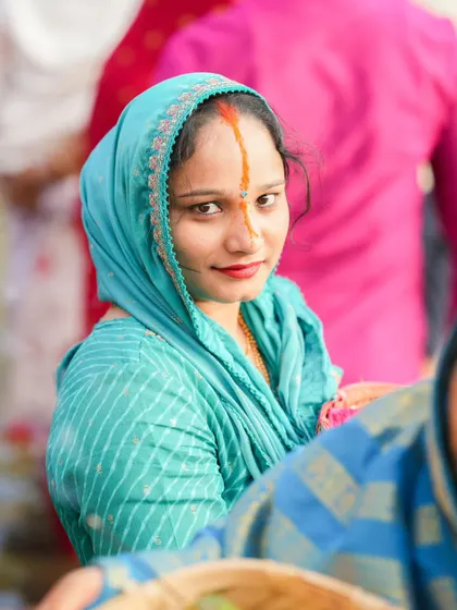 A young woman in a beautiful blue saree smiles at the camera during the Chhath Puja celebrations. The festival is also a time for community bonding and joy.
