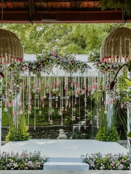 The wedding mandap at The Tamarind Tree, featuring clean white lines, traditional banana leaf pillars, and a backdrop of delicate pink and white floral tassels.