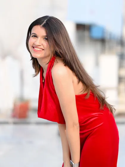 A happy and radiant portrait of a model in a red velvet dress, shot on a rooftop with a blurred city background.