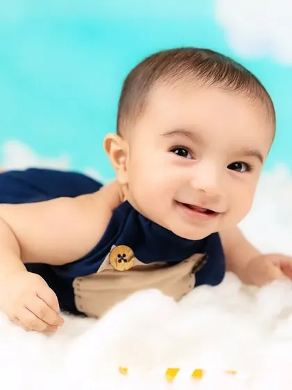 A happy baby boy lies on a bed of clouds, looking up with a bright smile. A dreamy and imaginative portrait.
