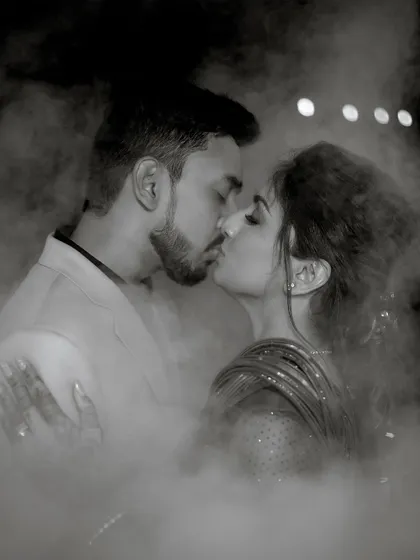 A romantic and dreamy black and white photo of Sushma and Athmic sharing a kiss amidst the fog during their Sangeet night.