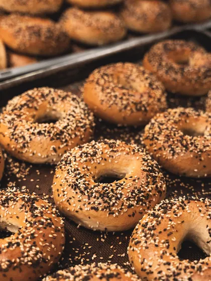 A fresh batch of our hand-rolled bagels, straight from the oven. We boil them before baking to achieve that classic shiny crust and dense, chewy interior. Topped generously with sesame seeds, they are a breakfast favorite.
