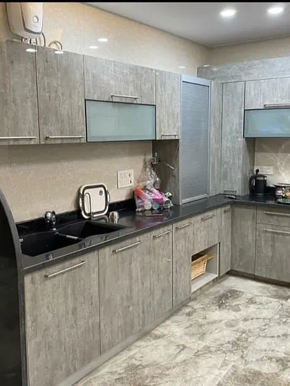 This kitchen uses a grey wood-grain laminate for a rustic yet modern look. The curved black granite countertop adds a unique design flair to the L-shaped layout.