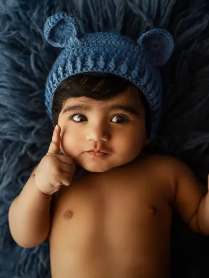 A playful baby boy wearing a cute bear-ear hat. Props like these add a touch of whimsy and fun to sitter sessions.