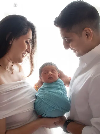 Welcoming their newborn with so much love. The parents' adoring smiles and the baby peacefully wrapped in blue create a perfect first family photo.