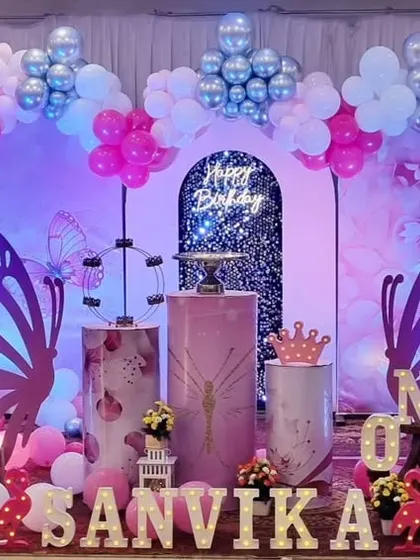 A stunning butterfly-themed first birthday setup with a shimmer wall backdrop, large marquee 'ONE', and beautiful pink and silver balloon decorations.