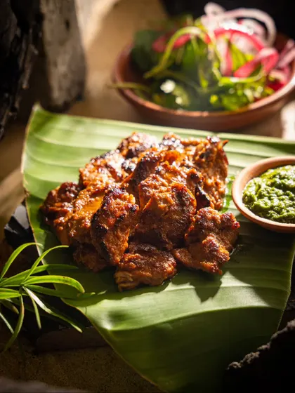Grilled meat served on a banana leaf with green chutney. We often use dark, moody lighting to create a dramatic effect for grilled and roasted dishes.