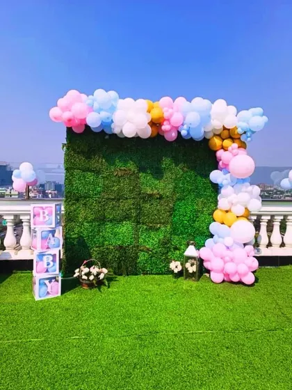 An outdoor photo booth with a lush green wall, a pastel balloon garland, and "BABY" blocks for a sunny rooftop baby shower.