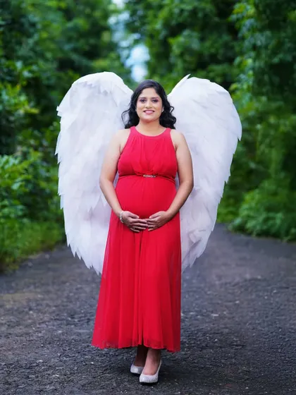 A whimsical and beautiful portrait using large angel wings as a prop. This outdoor shot in a natural setting creates a magical and ethereal look for the mother-to-be.