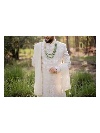 A detail shot focusing on the groom's elegant white sherwani and green beaded necklace.