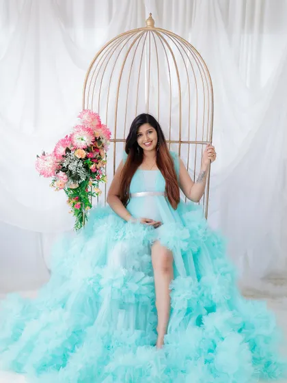A fairytale portrait in a stunning light blue gown. The mom-to-be is seated in a golden birdcage chair, looking like a princess.