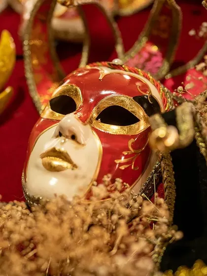 A close-up of a dramatic red and gold Venetian mask, nestled in dried baby's breath. This detail shot captures the texture and ambiance of the past that we recreated for a memorable cocktail party.