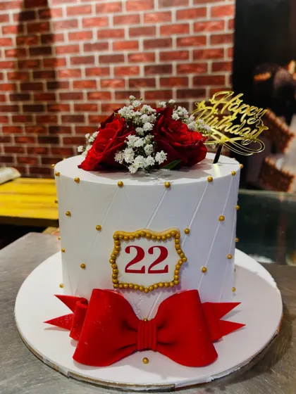 A chic white cake for a 22nd birthday, featuring a large red bow and fresh red roses.