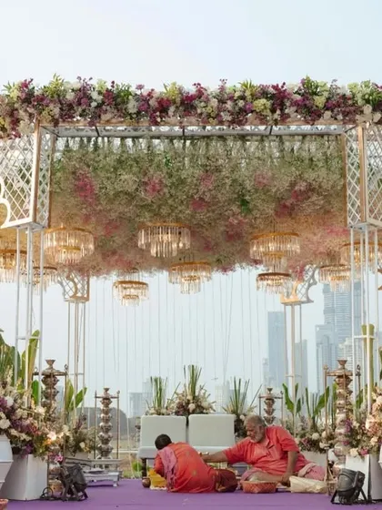 A delicate and dreamy mandap setup featuring a soft purple carpet, a canopy of baby's breath, and elegant white arches. The transparent ghost chairs add a touch of modern sophistication.
