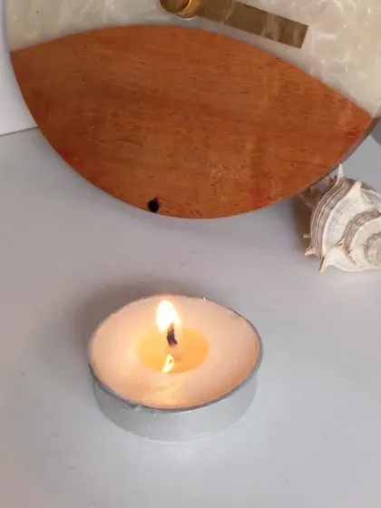 The same peach-scented tealight, now lit and casting a warm, cozy glow. The scent is soft and juicy, perfect for relaxation.