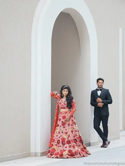 A stylish, full-length portrait of Nikita and Dhananjay. Her vibrant floral lehenga and his classic suit are framed by the clean white archway for a modern, editorial feel.