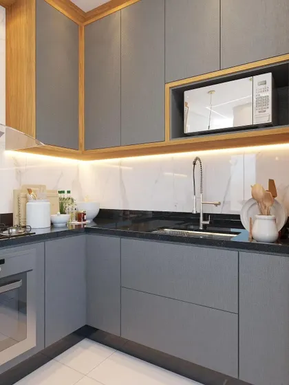 A close-up of the handle-less grey cabinetry and built-in microwave nook. The under-cabinet lighting illuminates the marble-effect backsplash and countertop, highlighting the clean lines and modern aesthetic of this kitchen design.