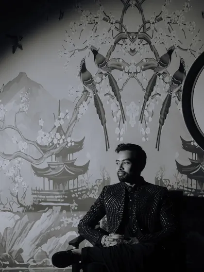 An artistic black and white portrait of the groom seated against a wall with a beautiful mural, using shadows and light to create a dramatic effect.