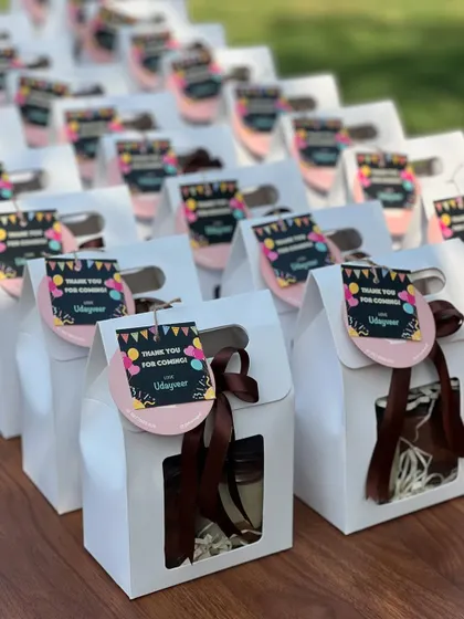 Fun and festive return favours for a birthday party. These white gable boxes hold a dessert jar and are decorated with a colourful, personalized "Thank You" tag and a simple brown ribbon.