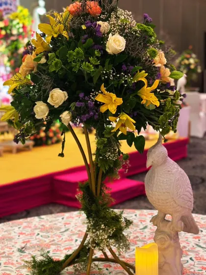 A rustic yet elegant centerpiece for a Mehendi brunch, featuring a tall floral arrangement and a whimsical bird statue.