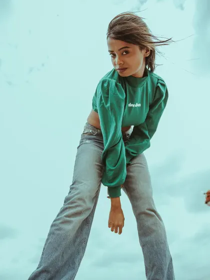 Model in a green crop top leaning forward, looking at the camera with a confident expression