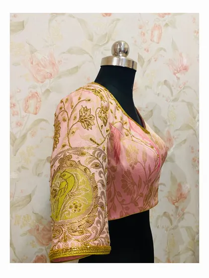 A delicate baby pink blouse with intricate bird and floral motifs embroidered in gold thread. The design on the back is just as beautiful as the front.