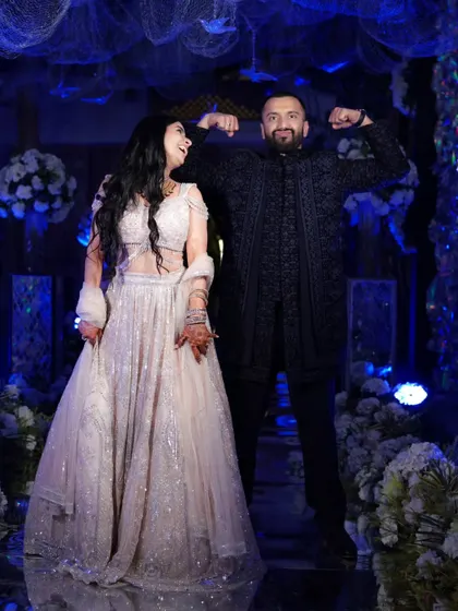 A fun, candid shot of the couple, with the groom flexing playfully, capturing the lighthearted and joyful spirit of their Sangeet night.
